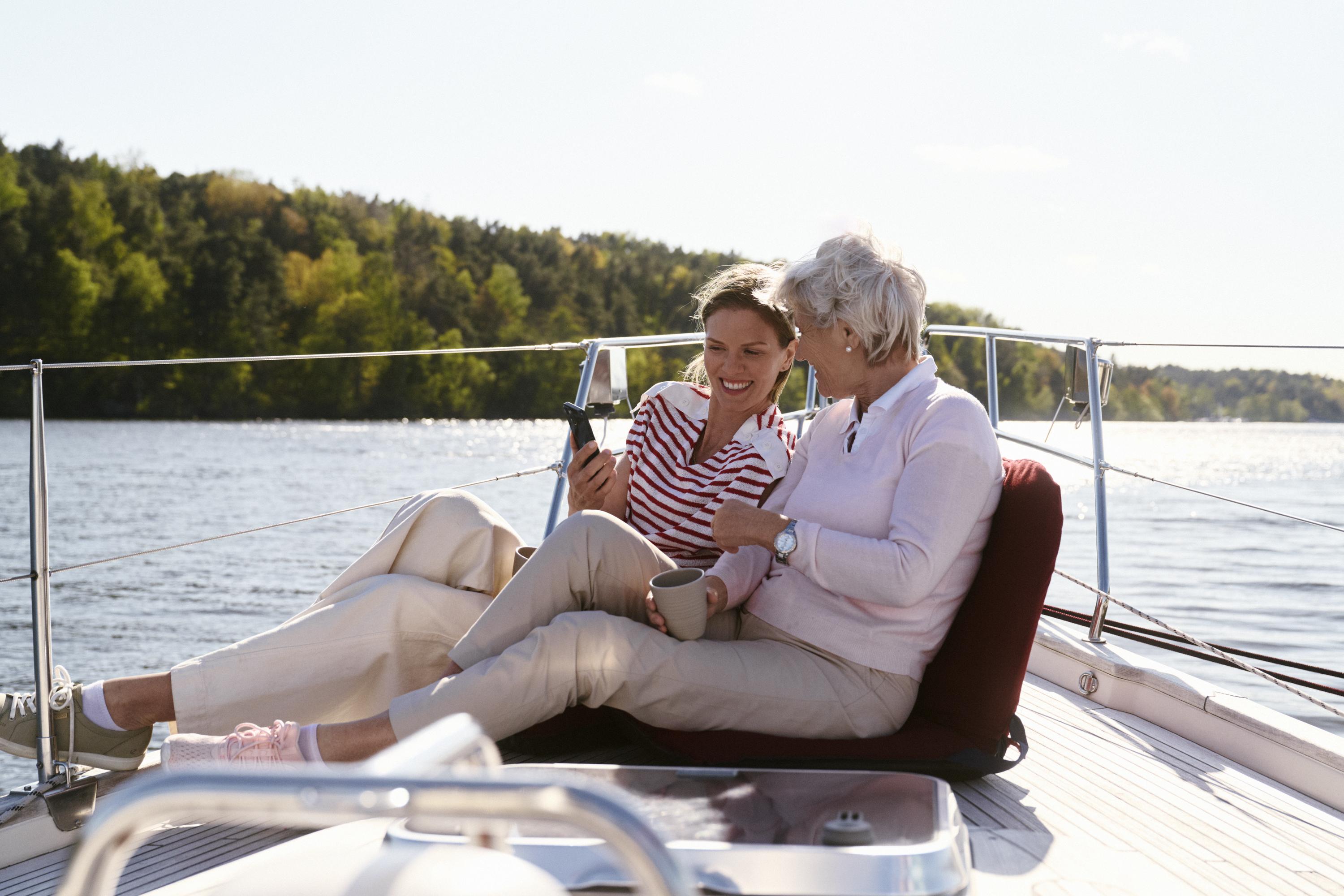 Två kvinnor kollar i en mobil tillsammans på en segelbåt