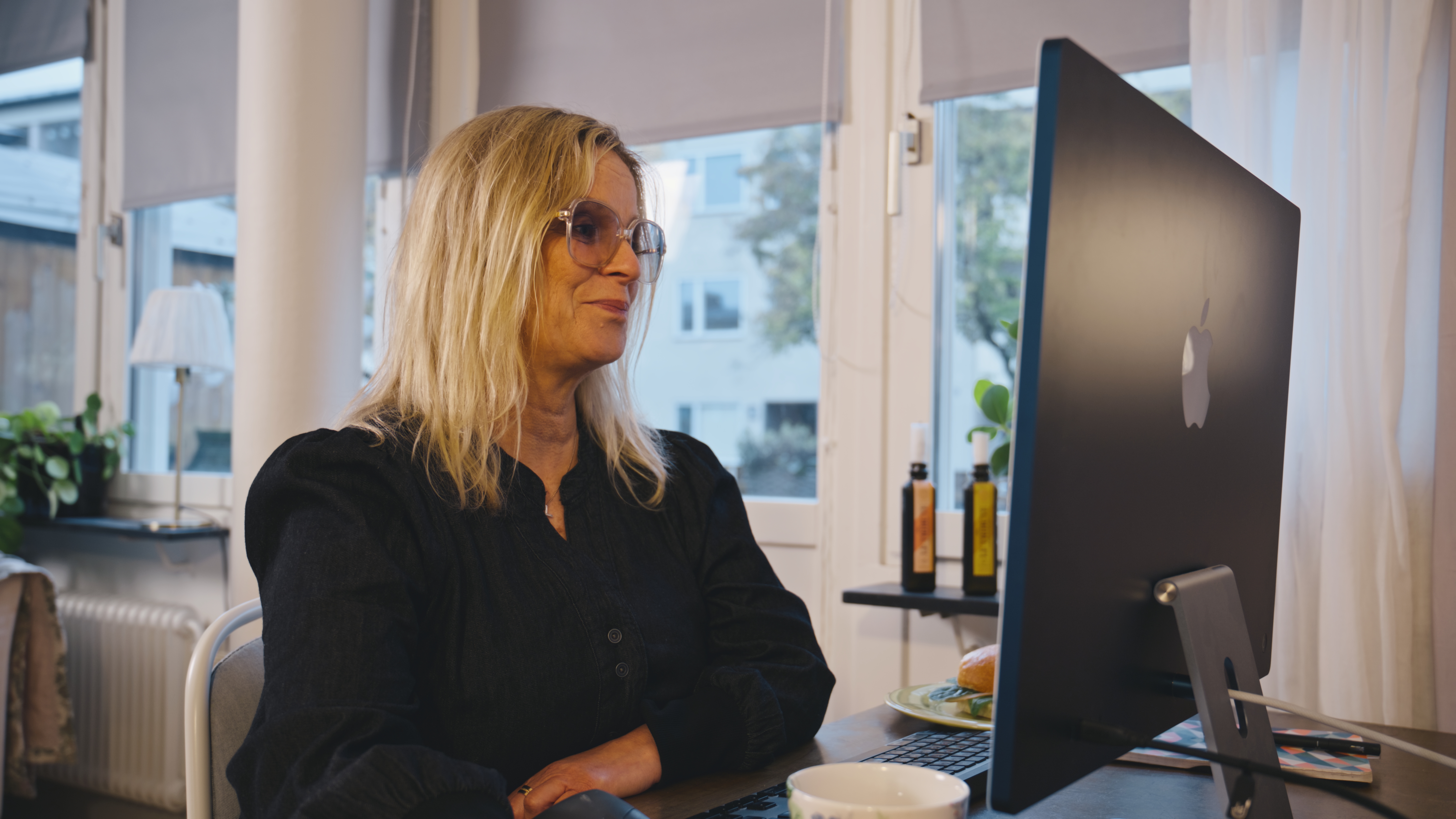 kvinna med blont hår och glasögon sitter hemma vid sin dator