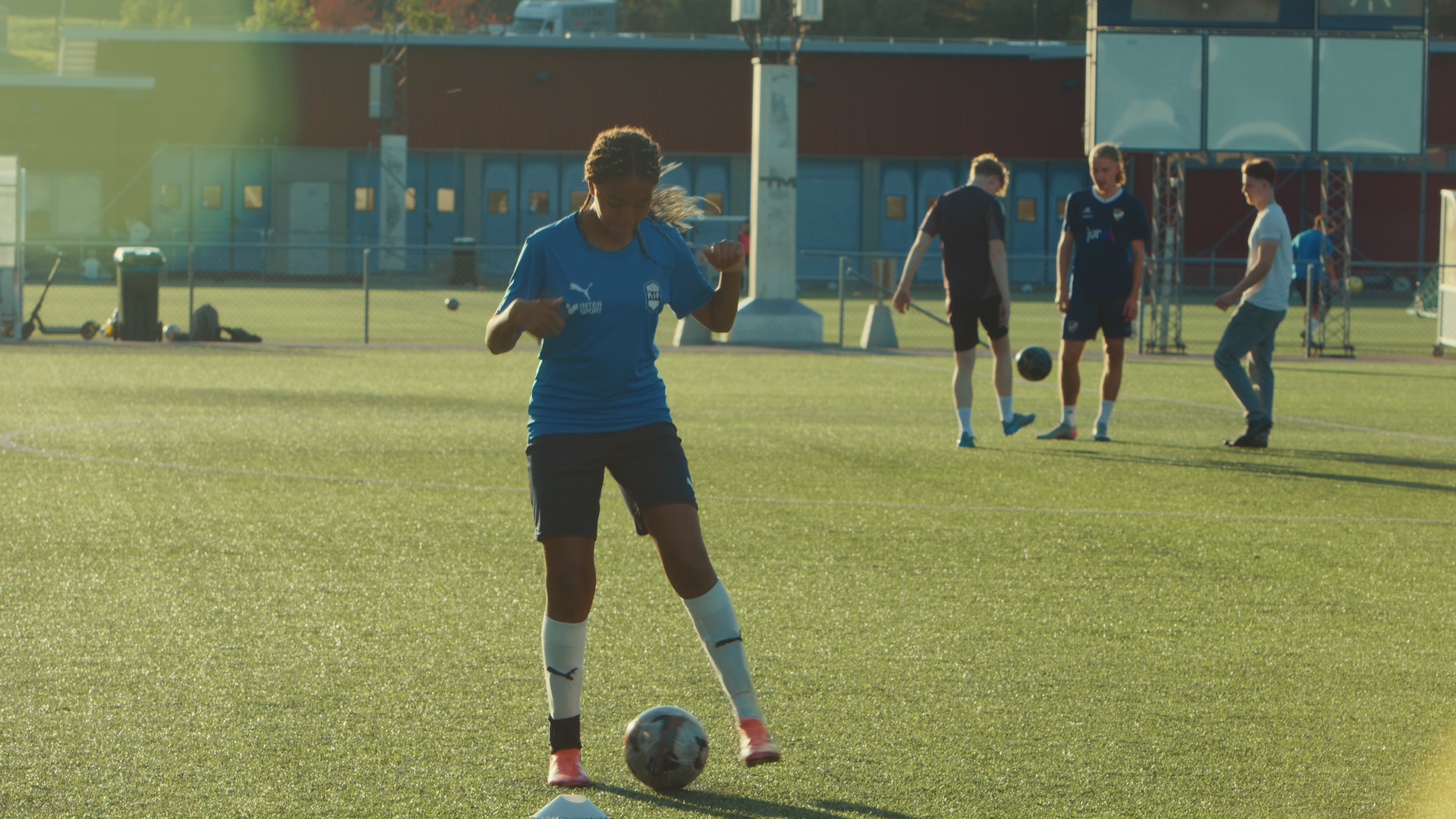 en tonårstjej med fotboll, i bakgrunden tre killar med boll