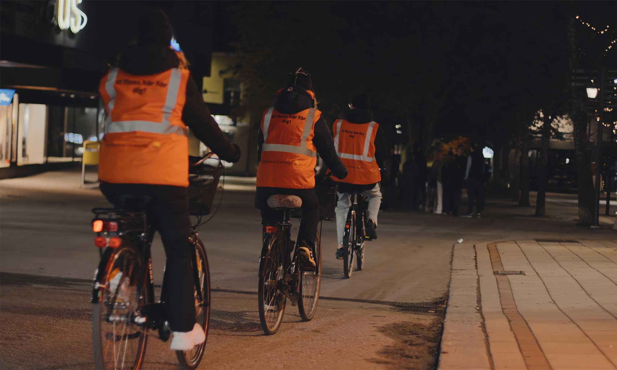 Tre personer på cyklar bärandes orangea västar med texten vi finns här för dig