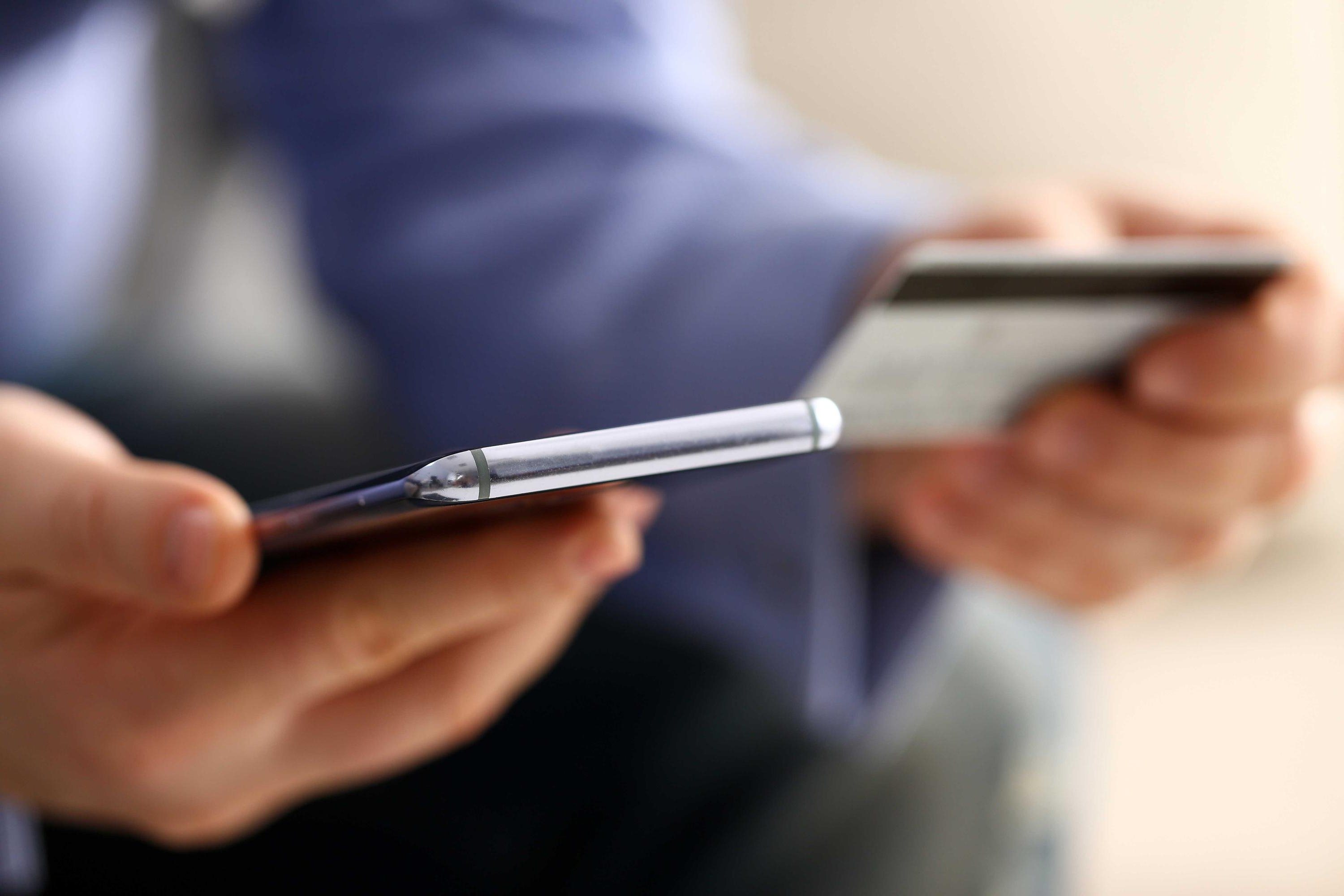Man med blå skjorta håller i en mobiltelefon samt ett betalkort