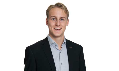 man iklädd grå skjorta och mörk kavaj ler mot kameran