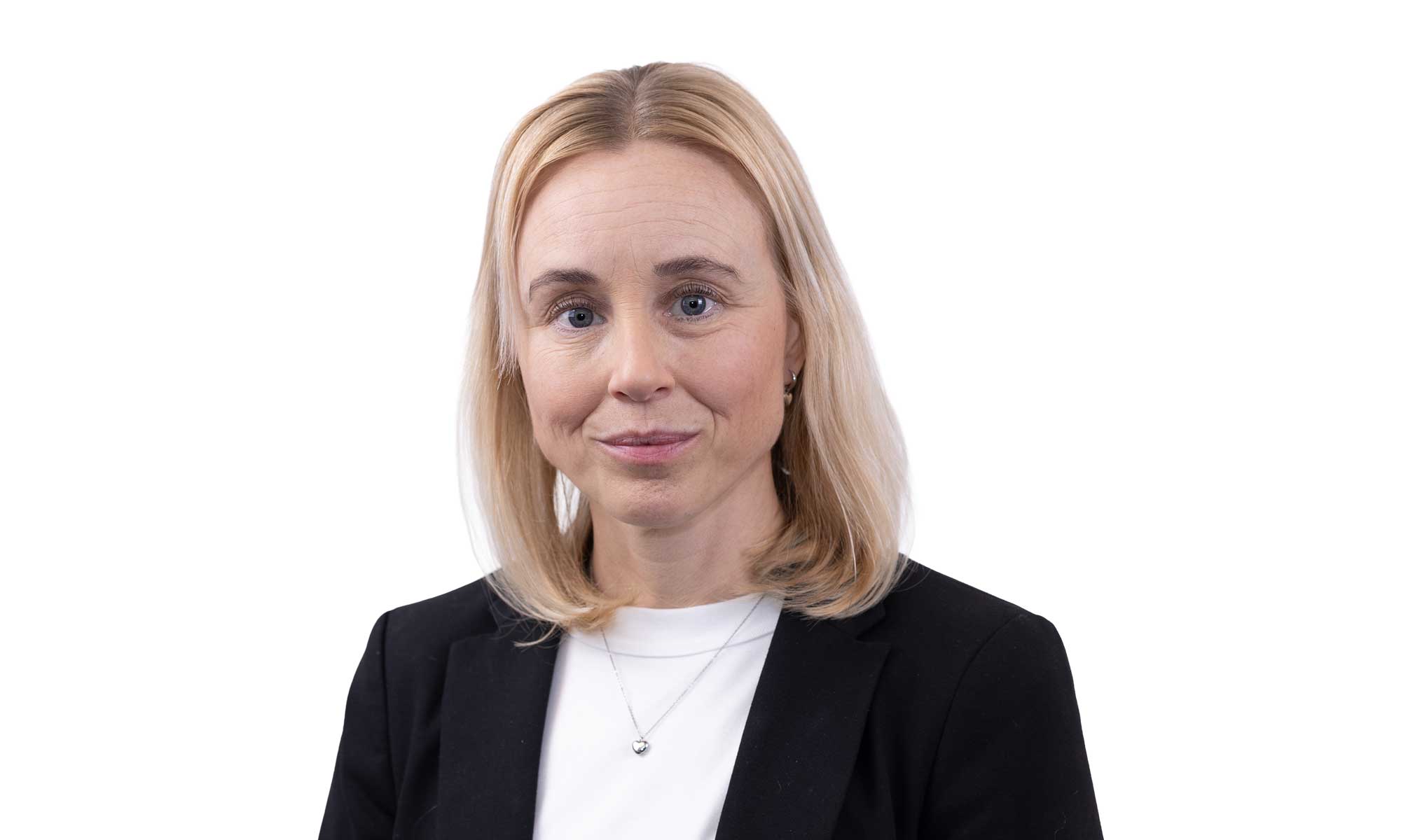 a women with blond hair dressed in a white shirt and a black jacket is looking into the camera
