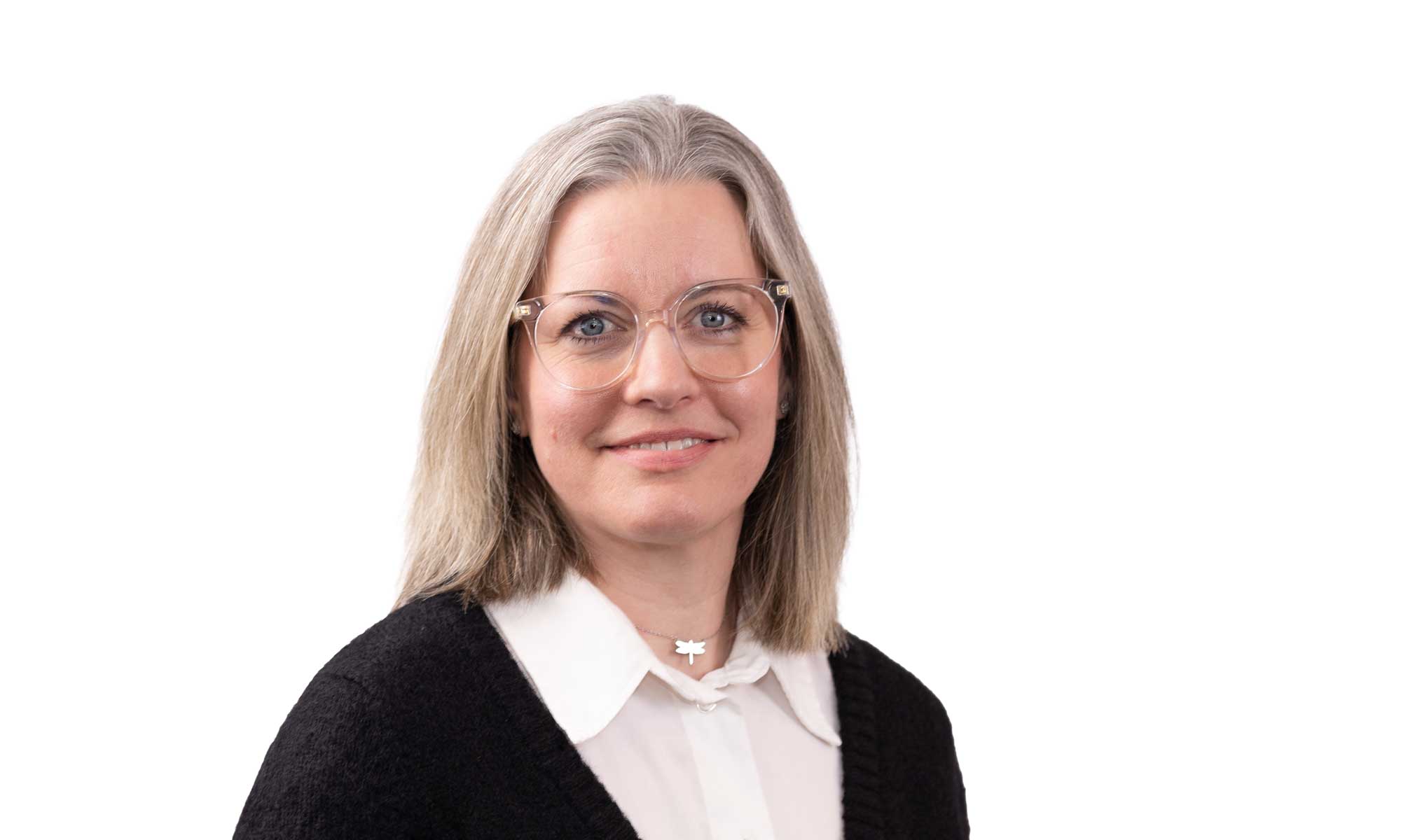 a women with blond hair dressed in a white shirt and a black jacket is looking into the camera