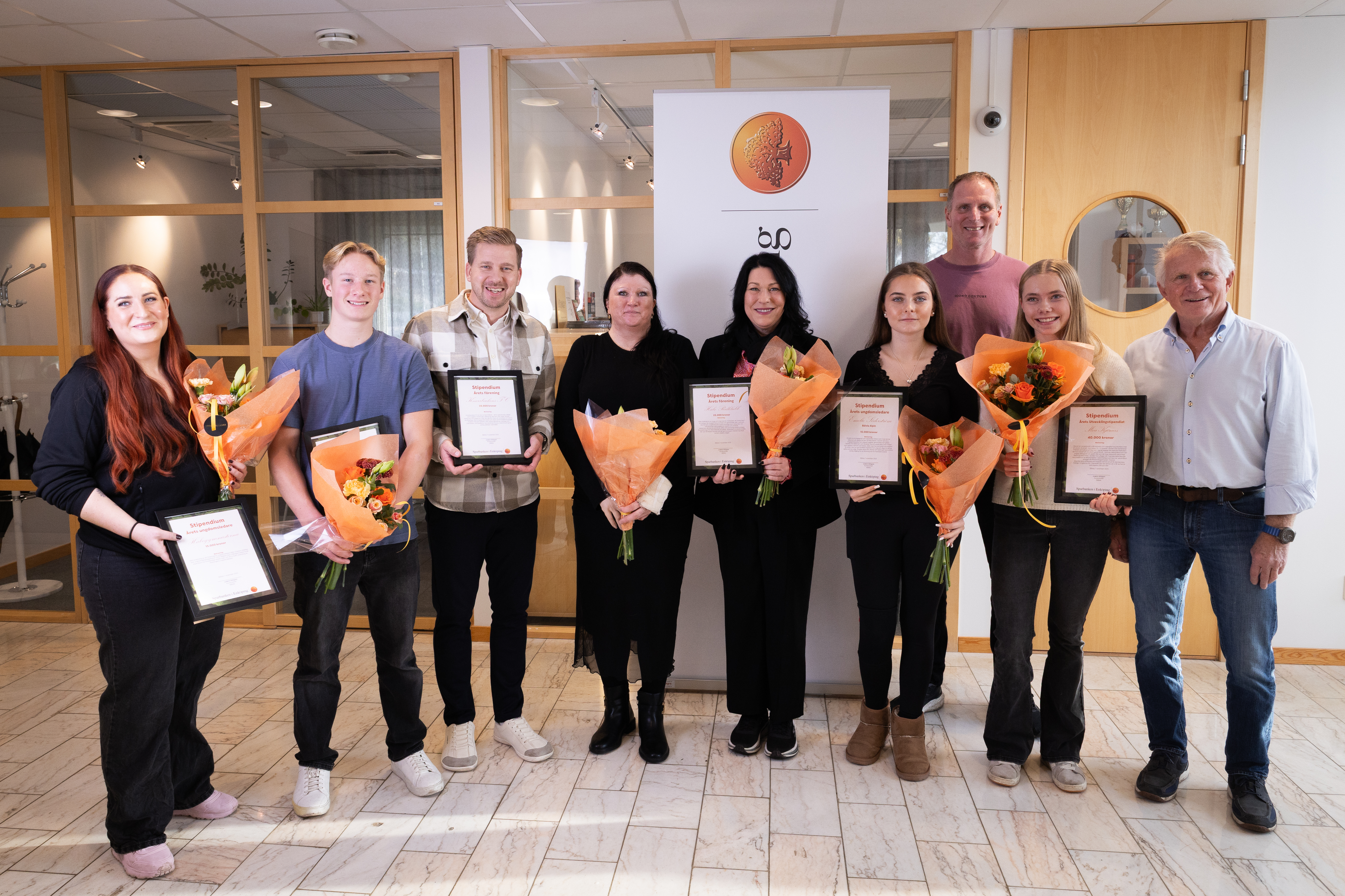 9 personer hållandes inramade stipendier samt blombuketter