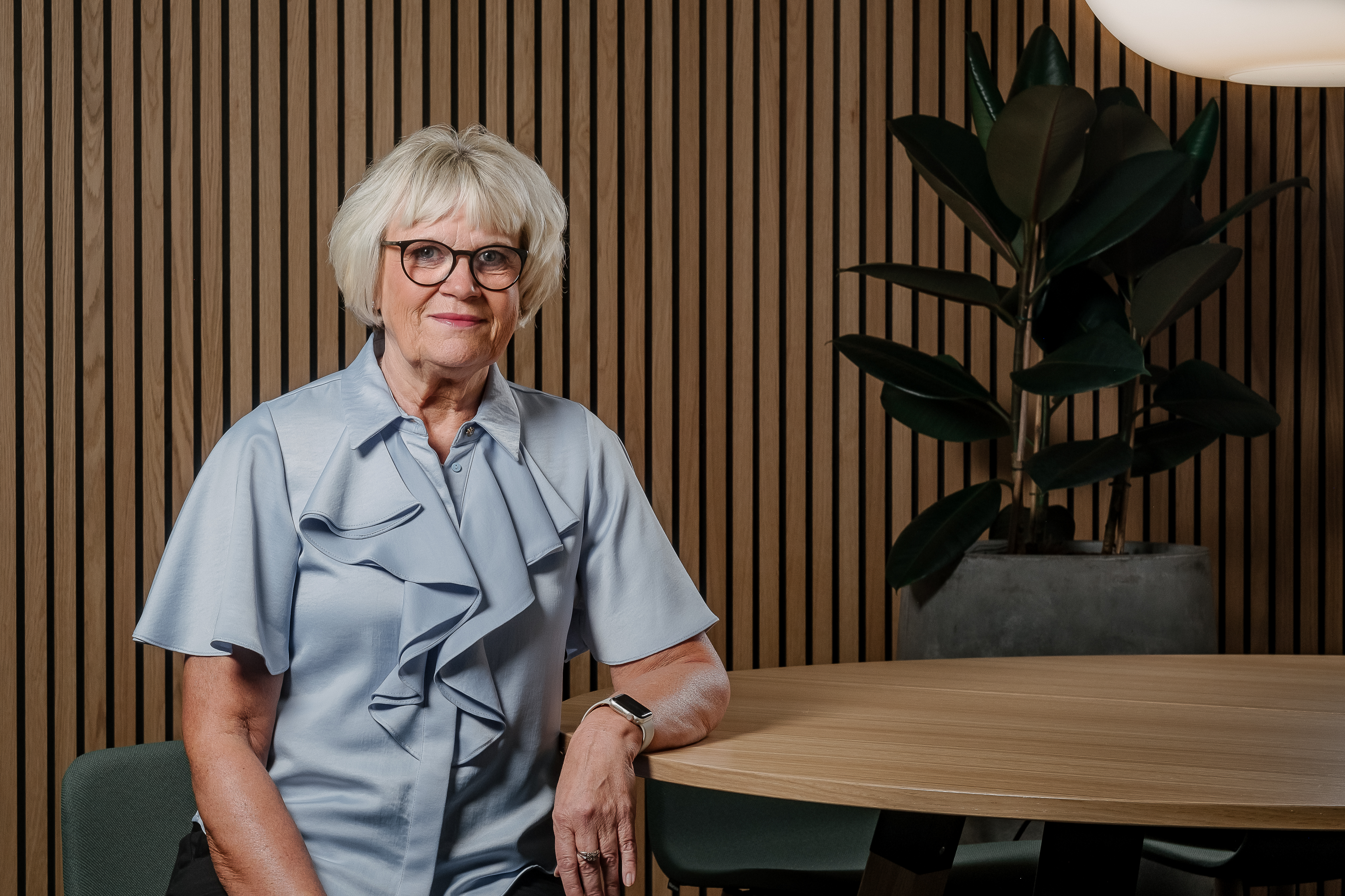 En kvinna klädd i blå blus lutar sin armbåge mot ett bord