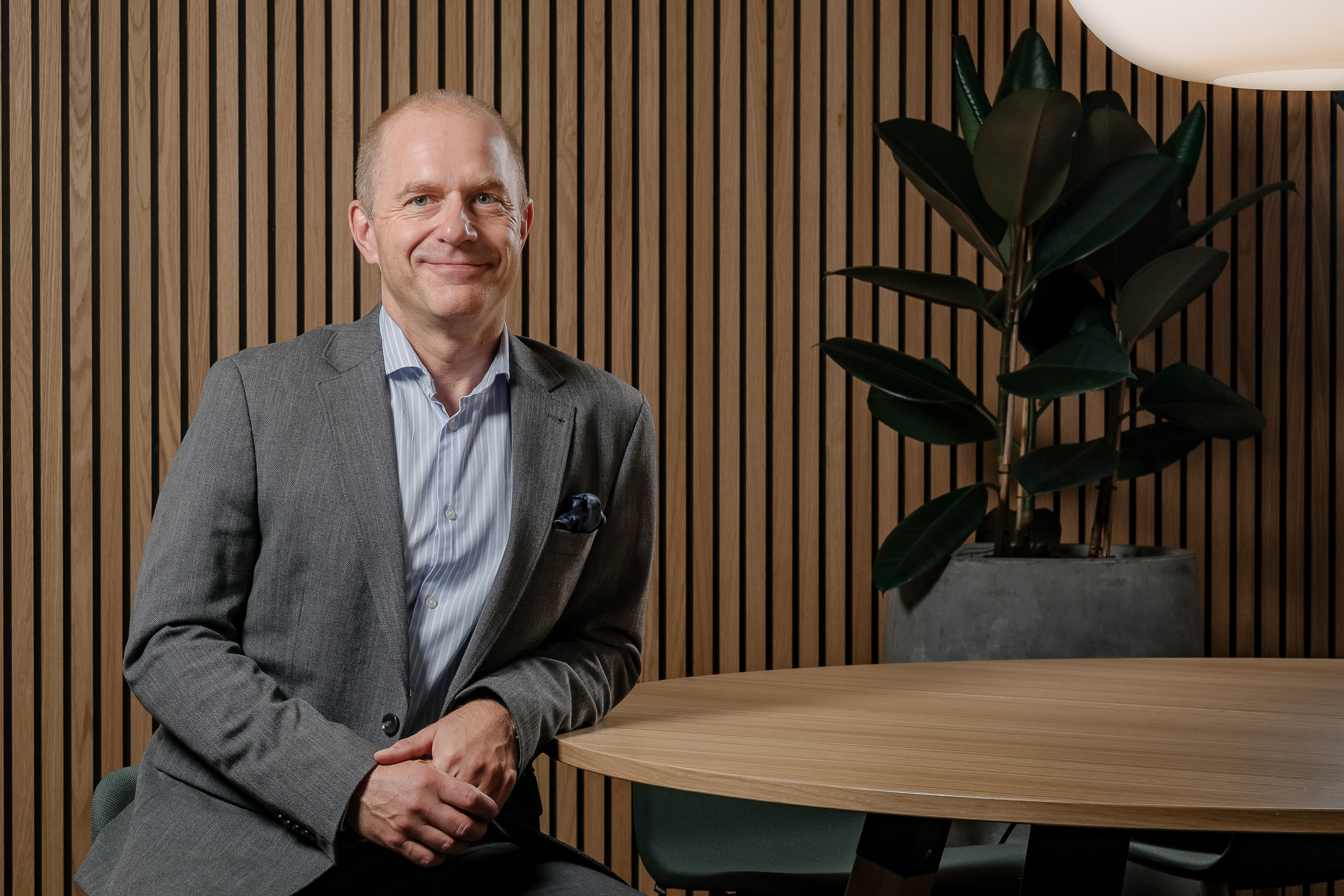 En man iklädd grå kostym lutar sin arm mot ett runt bord